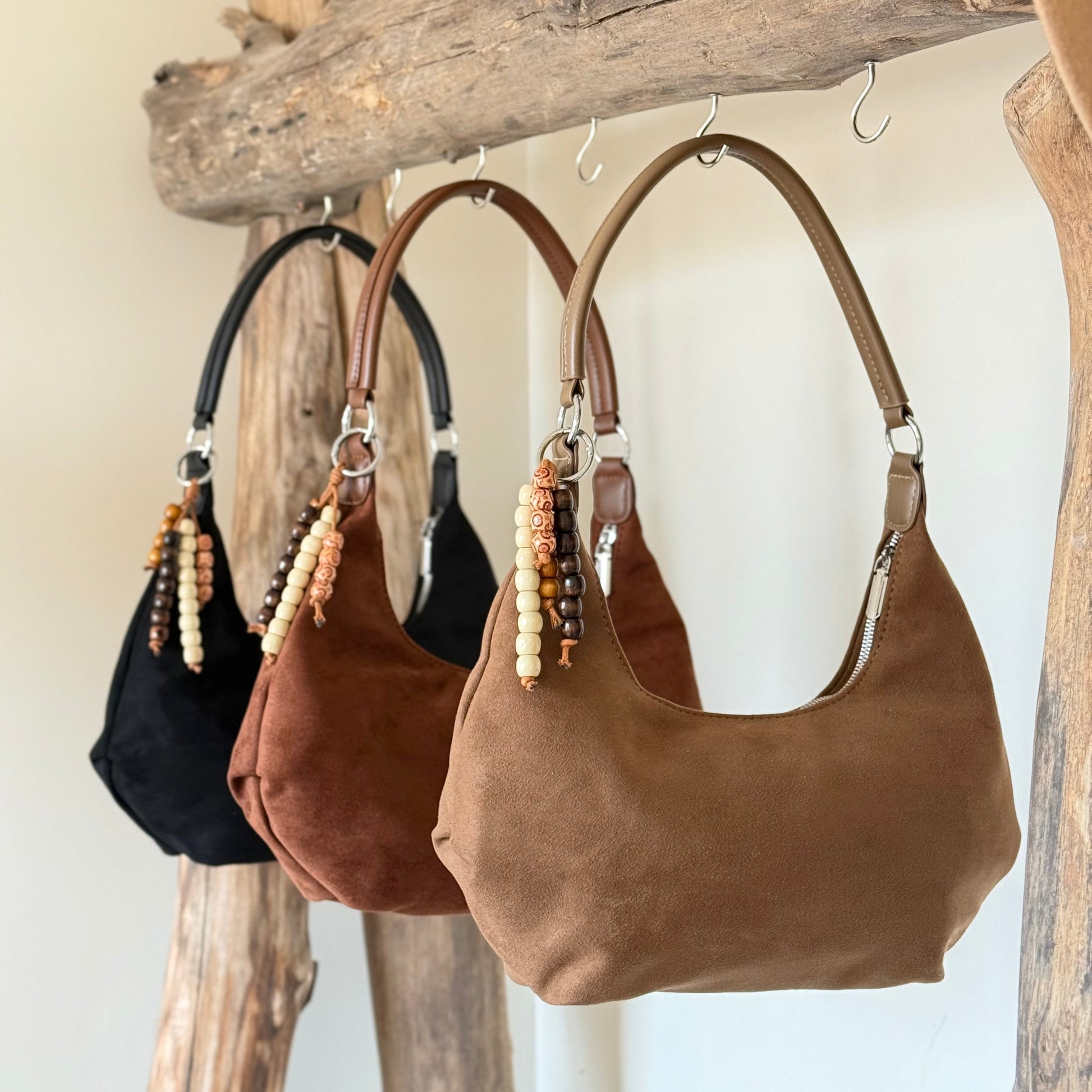 Suede handbags in black, brown, and beige hanging on a wooden rack.