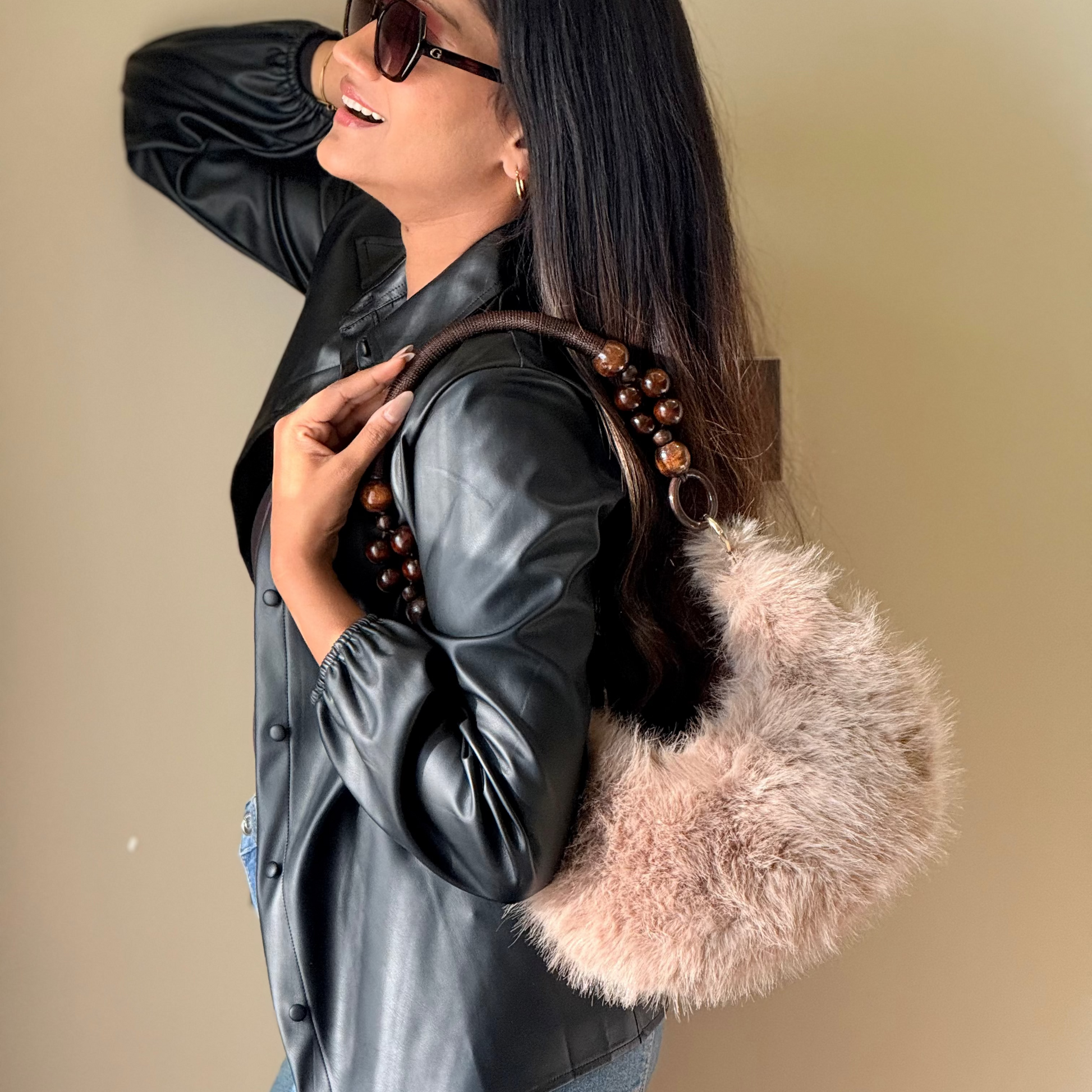 Woman wearing a black leather jacket with a fur-lined handbag against a beige background